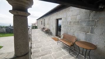 A stone building with a covered patio area, featuring stone flooring, a bench, and two wicker tables.