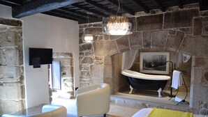A modern bathroom with a stone wall, a bathtub, a white chair, and a flat-screen TV. - Reitoral de Parada (Parada de Sil)