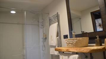 A bathroom with a glass shower enclosure, a wooden vanity with a soap dispenser, and a towel rack with towels.
