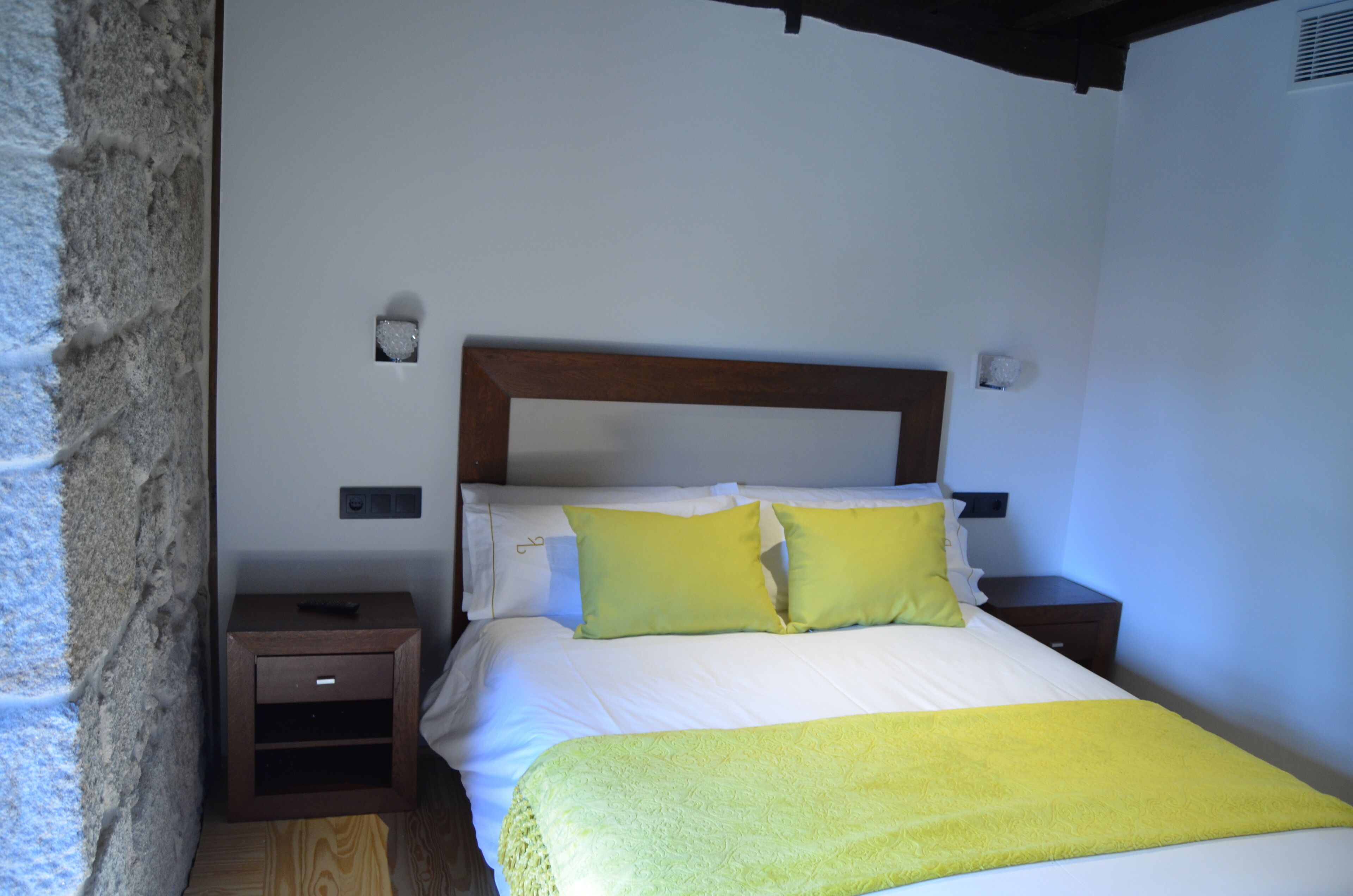 Un dormitorio con cabecera de madera, ropa de cama blanca y dos mesitas de noche con lámparas.