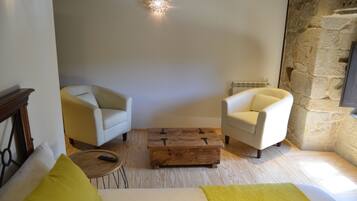 A cozy room with two white armchairs, a wooden coffee table, and a bed with a yellow throw.