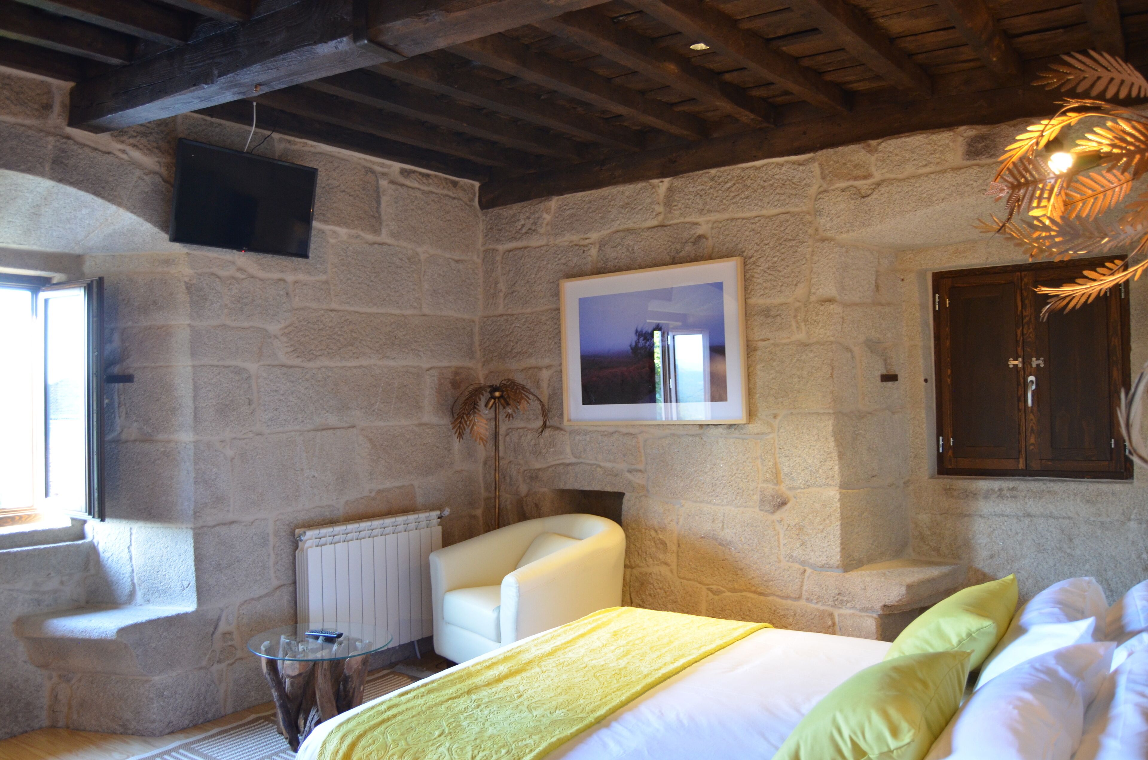Un dormitorio con paredes de piedra, una cama, un sillón blanco, una mesita y una chimenea.