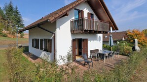 Ein zweistöckiges Haus mit Balkon, einer Terrasse, einem Tisch und Stühlen sowie einer Satellitenschüssel.