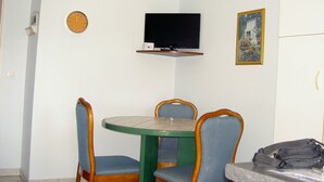 A small dining area with a round table and four chairs, a television mounted on the wall, and a framed picture above the table. - Attached ground floor apartment on Enclosed grounds (Plouay)