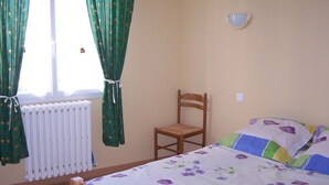 A bedroom with a bed, a chair, a radiator, and curtains. - Attached ground floor apartment on Enclosed grounds (Plouay)