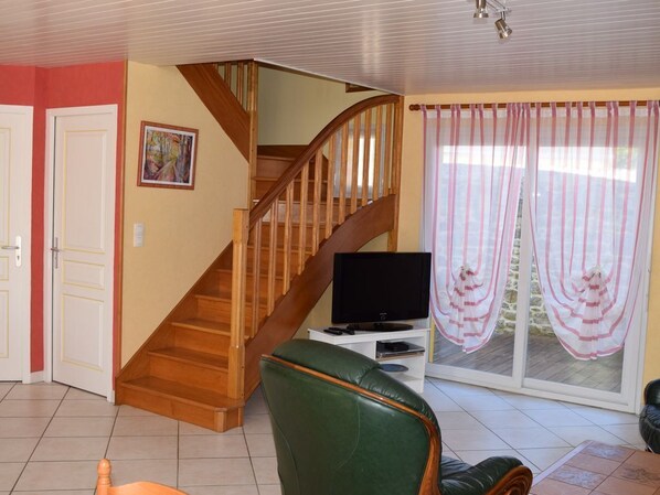A living room with a wooden staircase, a television on a stand, and a green chair.