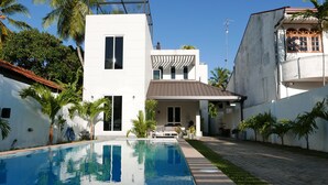 A modern house with a swimming pool, white exterior walls, and a covered patio area. - Design House in a famous area - St. Sebastian Curch & Temple road (Negombo/Katuwapitiye)