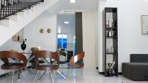 A modern living room with a staircase, a dining area with chairs, and a bookshelf. - Design House in a famous area - St. Sebastian Curch & Temple road (Negombo/Katuwapitiye)