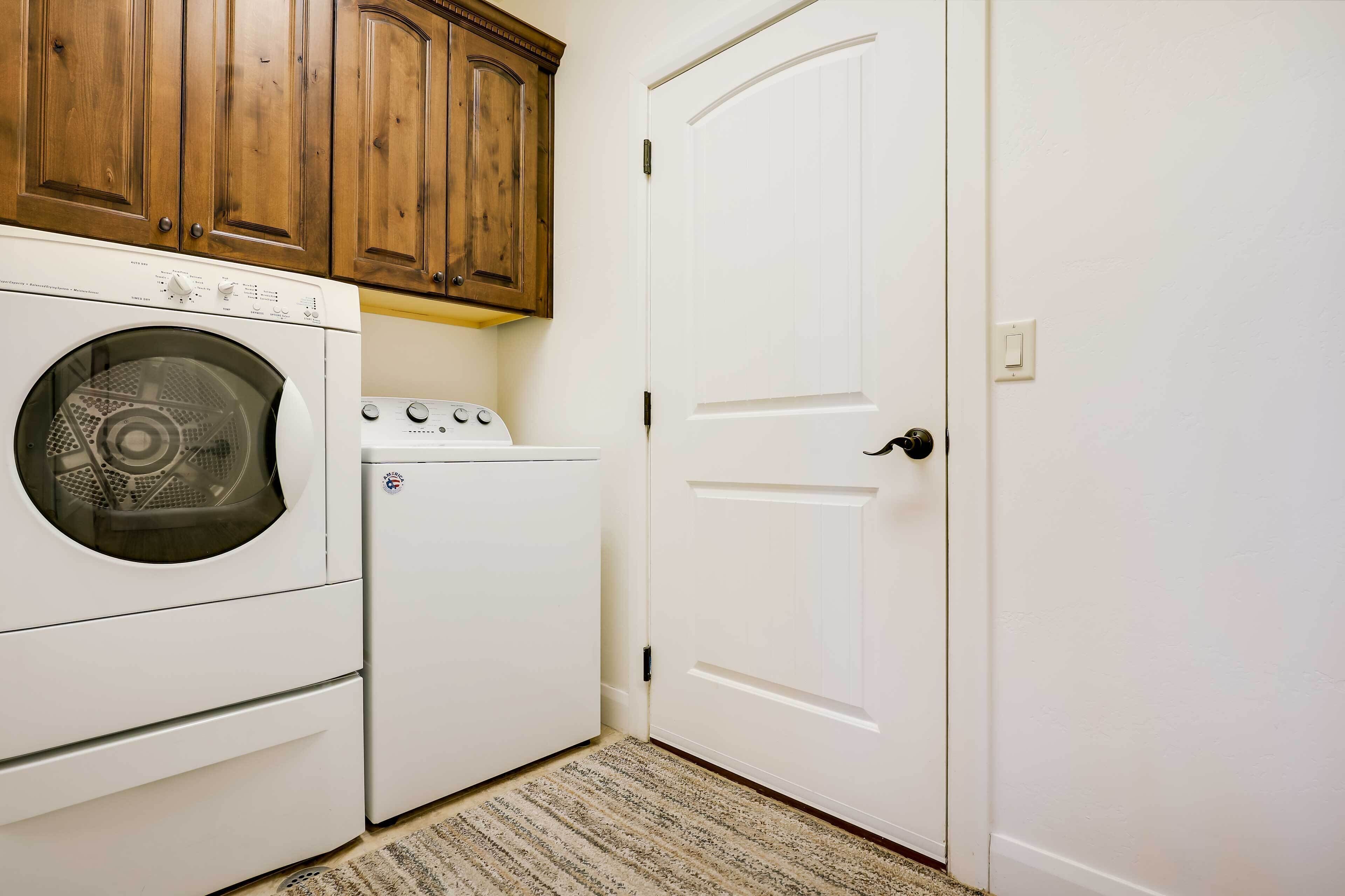 A laundry room with a front-loading washer and dryer, wooden cabinets above, and a white door.