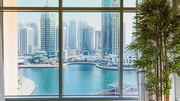 Vista desde una ventana que da a un puerto deportivo con edificios altos al fondo.
