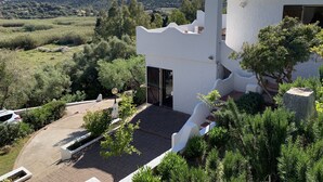 Un edificio blanco con techo de tejas, rodeado de vegetación y un paisaje montañoso.