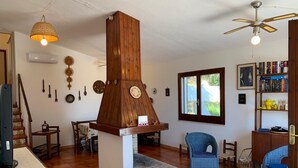 Una sala de estar con chimenea de madera, ventilador de techo, estantería y comedor.