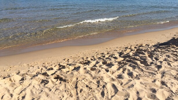 Una playa arenosa con agua cristalina y un promontorio rocoso al fondo.