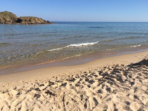 Une plage de sable fin, avec une eau cristalline et un promontoire rocheux en arrière-plan.