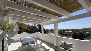 Un patio cubierto con muebles blancos, vistas del paisaje y techo de bambú.
