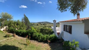 Un edificio blanco con tejado rojo, una torre pequeña y un jardín con diversas plantas y un sendero.