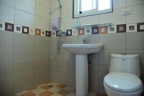 Ett badrum med ett vitt handfat, toalett och dusch. Väggarna är kaklade med ett mönster av kvadrater och rektanglar.