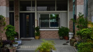 A building with a tiled facade, a black door, and multiple potted plants in front. - Happy feet Youth B&B (Hualien City)
