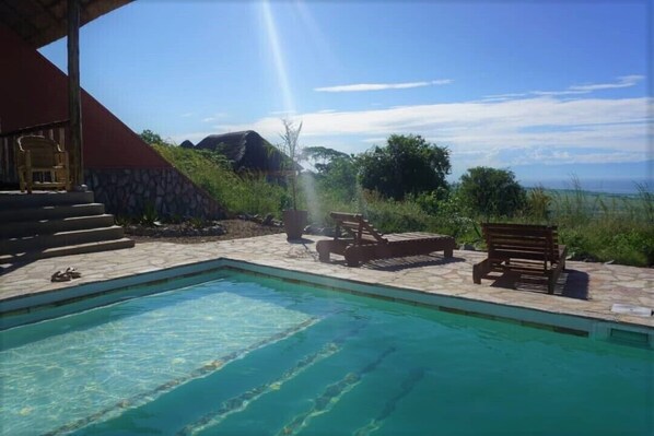 A pool area with clear water, surrounded by stone steps and wooden furniture.
