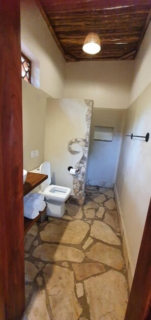 A bathroom with a stone floor, a toilet, a sink, and a shower area.