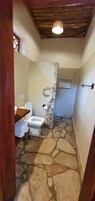 Ein Badezimmer mit Steinboden, einer weißen Toilette und einem Holzregal.