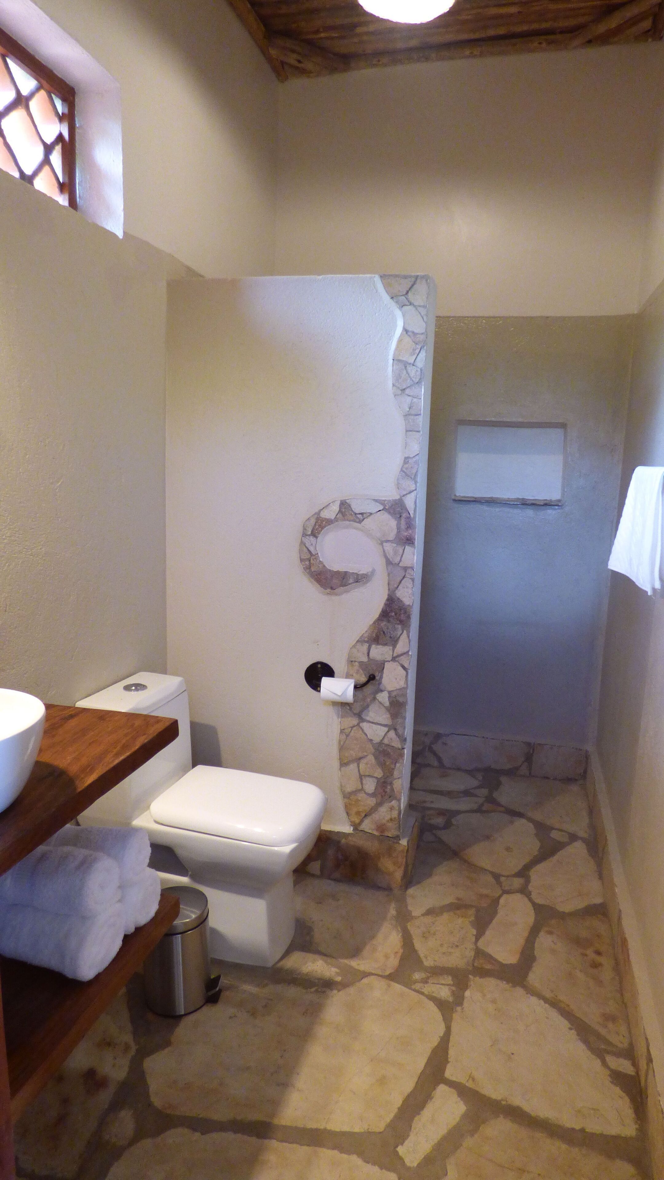 Un baño con piso de piedra, un inodoro, un lavamanos y una ducha con pared de piedra.