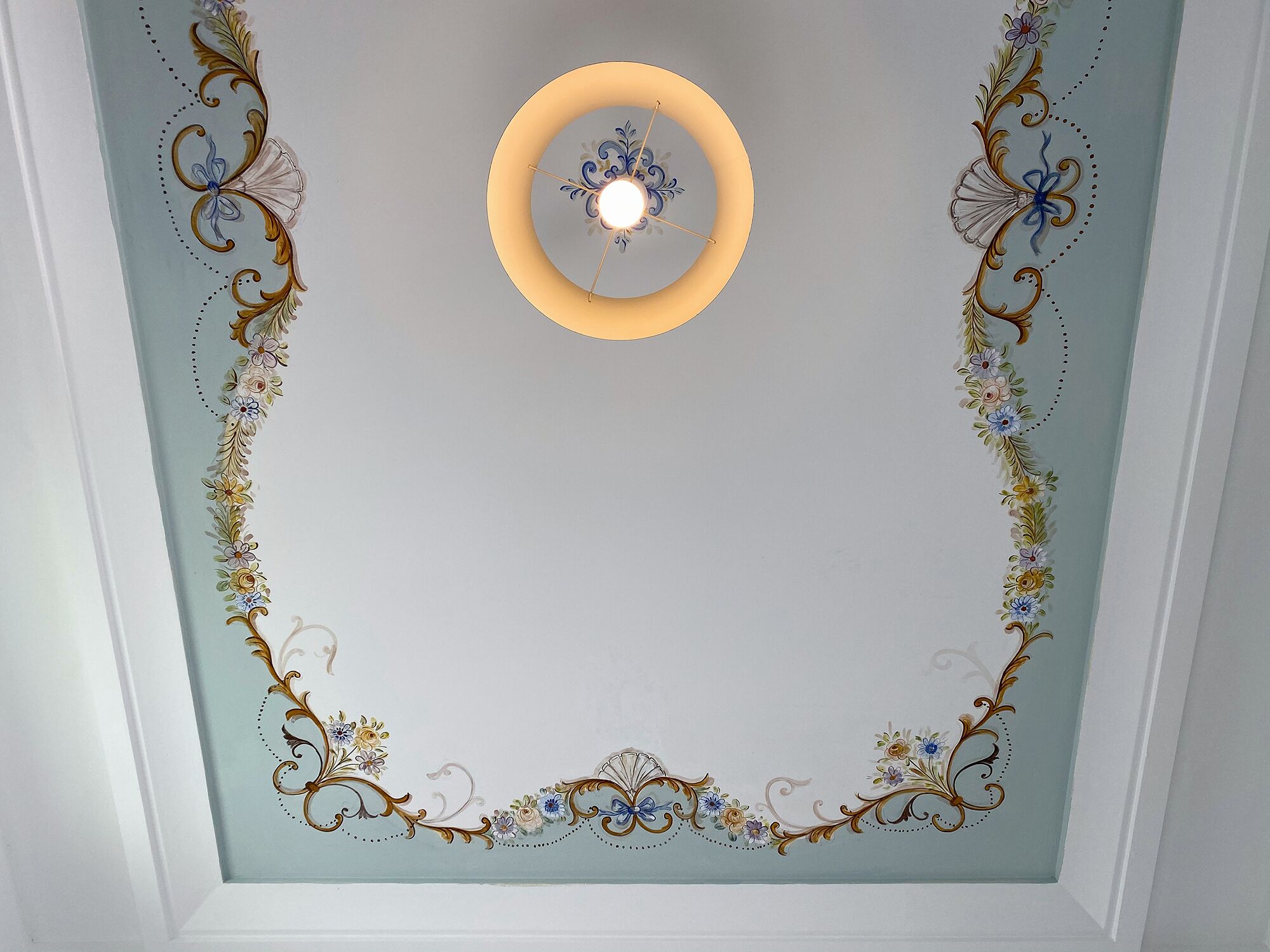 A ceiling with a central light fixture surrounded by ornate floral and scroll designs.