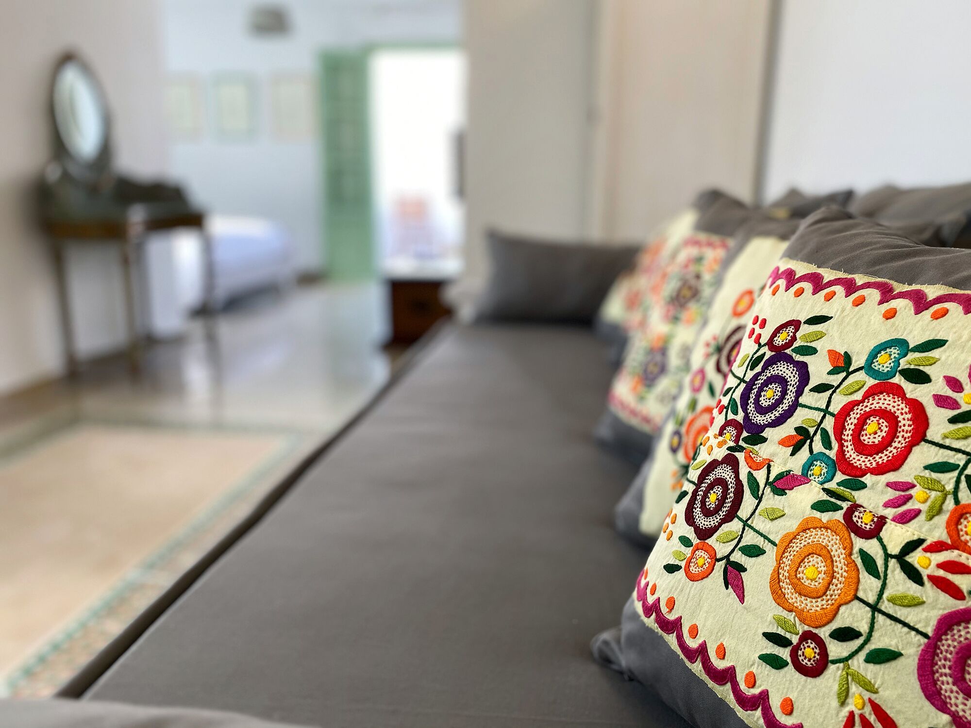 A row of sofas with colorful embroidered pillows, a mirror, and a bed in the background.