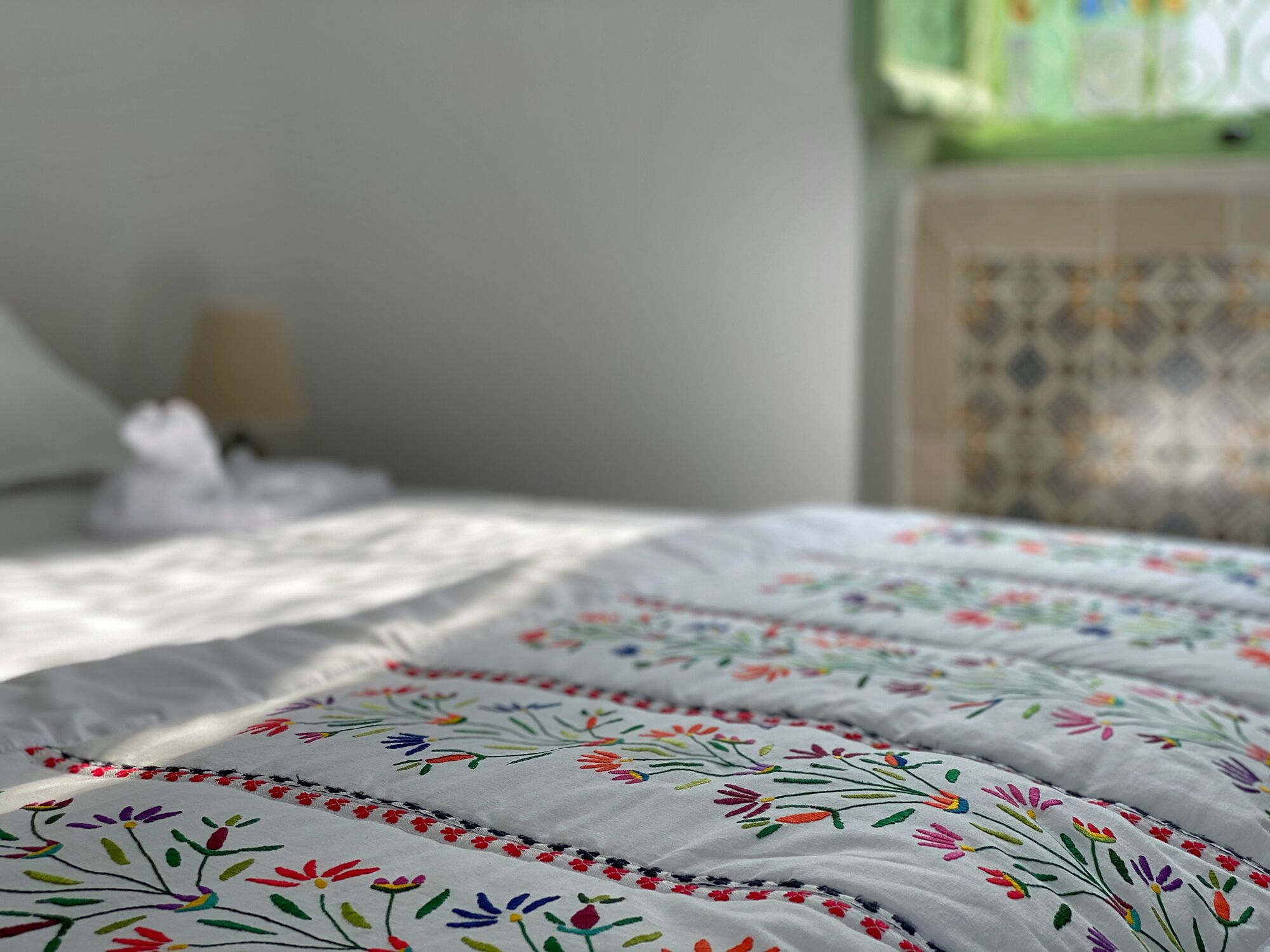 A bed with a white bedspread featuring colorful floral embroidery.
