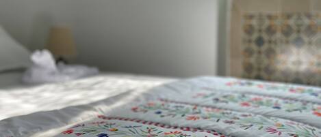 A bed with a white bedspread featuring colorful floral embroidery.
