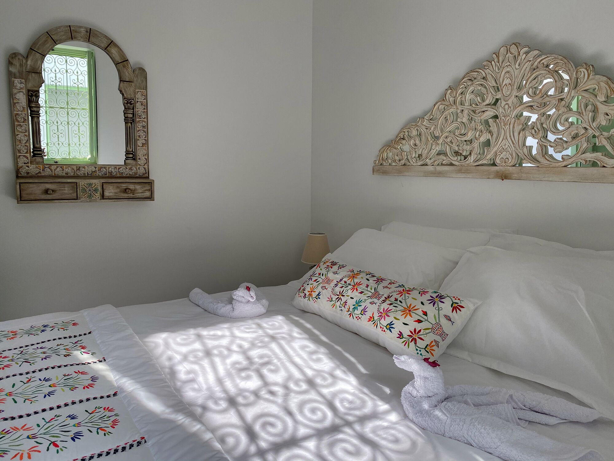 Ein ordentlich bezogenes Bett mit einem floralen Kissen, einem dekorativen Spiegel und einem Bettgestell mit aufwendigen Schnitzereien.
