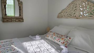 Ein ordentlich bezogenes Bett mit einem floralen Kissen, einem dekorativen Spiegel und einem Bettgestell mit aufwendigen Schnitzereien.