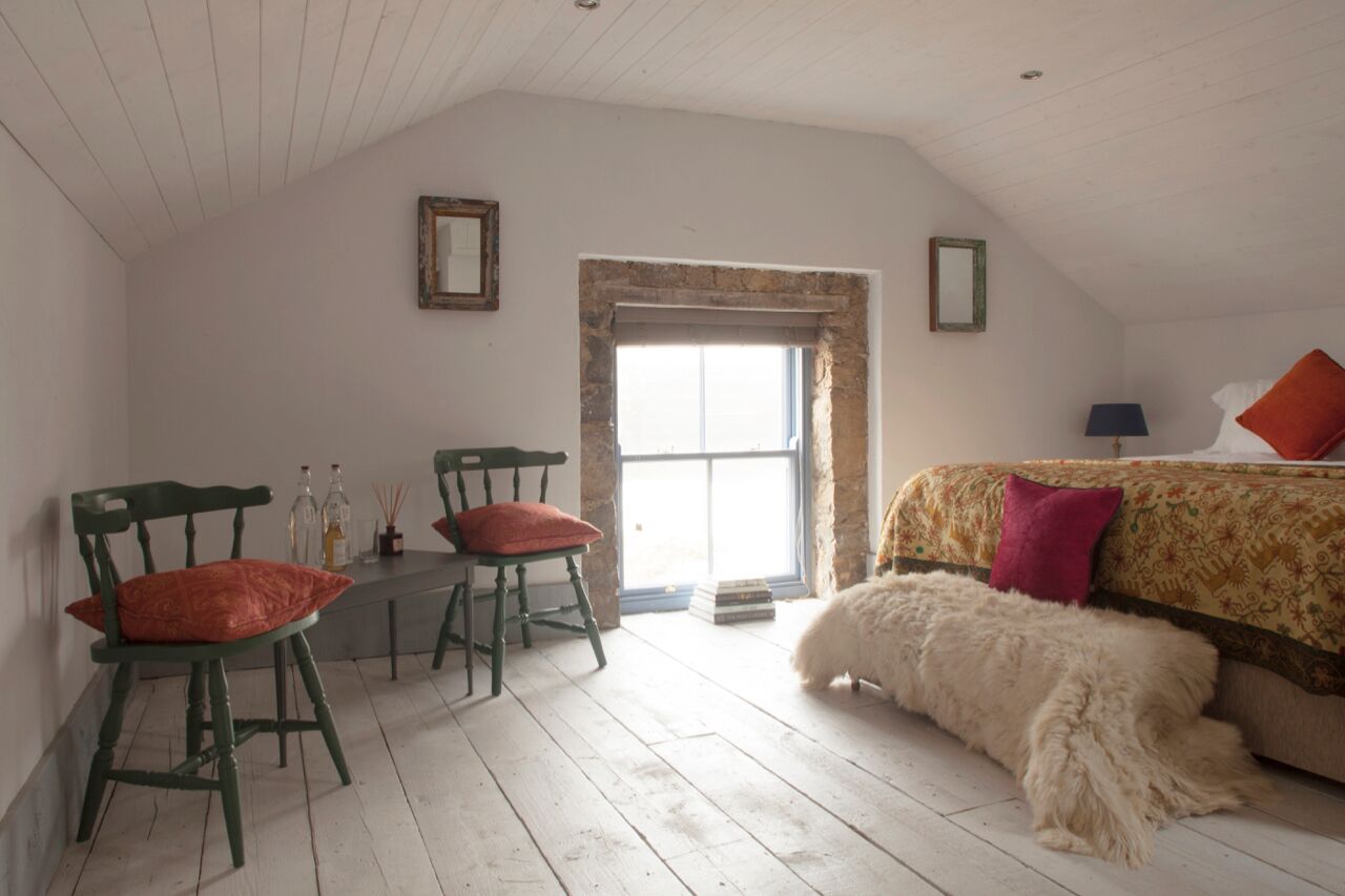 A room with a bed, a chair, a table, and a window.