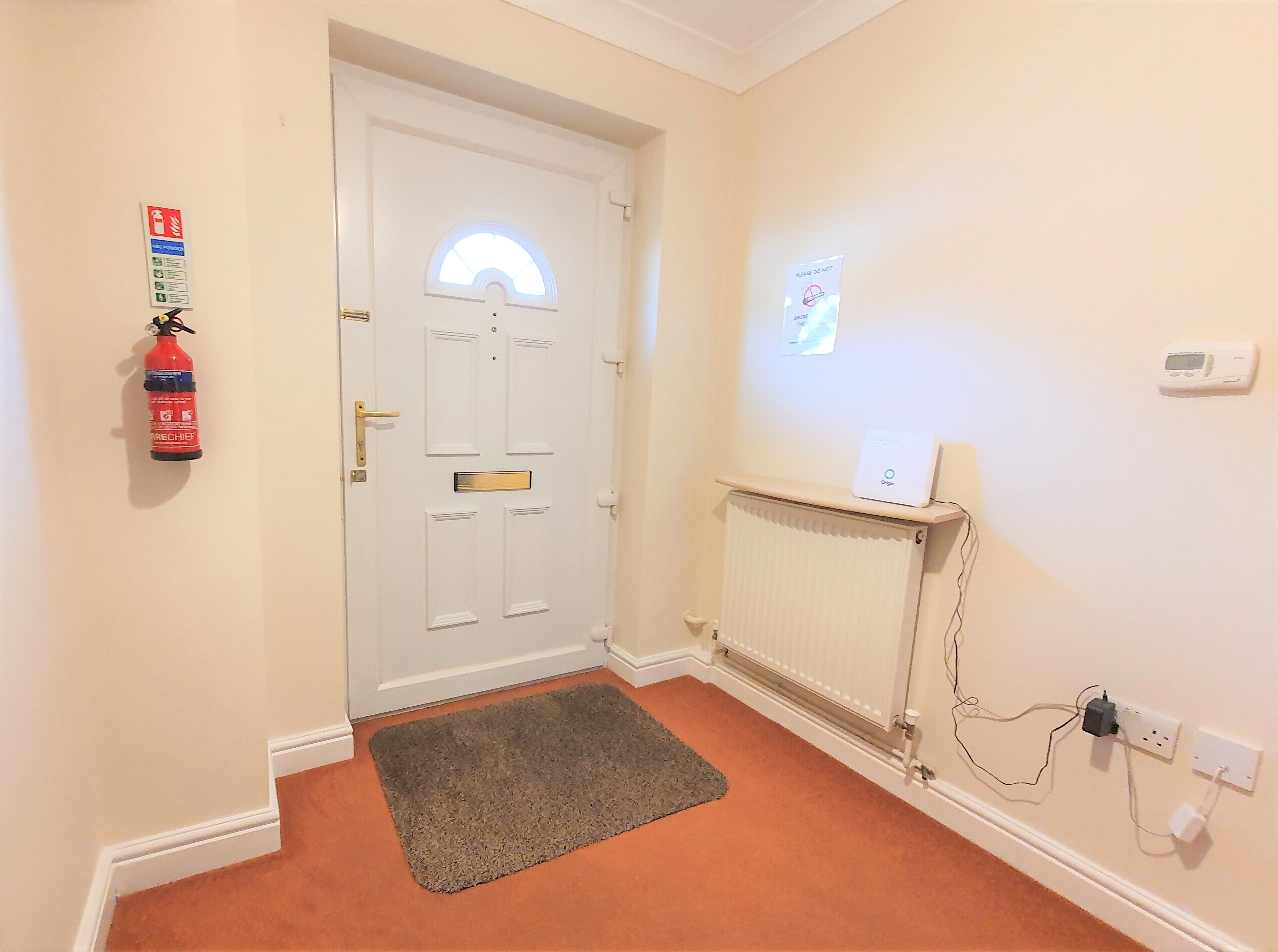 A hallway with a white door, a fire extinguisher, a thermostat, and a power outlet.