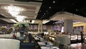 A modern restaurant with high ceilings, chandeliers, and a central display area. Tables are arranged for dining with a view of the kitchen in the background. - Grass Residences - Condo (Quezon City)