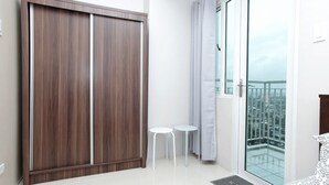 A modern bedroom with a sliding door, a small table, a chair, and a balcony with a city view. - Grass Residences - Condo (Quezon City)