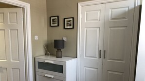 Een slaapkamer met een bed, een dressoir met lades, een lamp en twee deuren.
