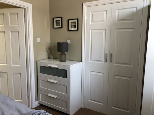 A bedroom with a bed, a dresser with drawers, a lamp, and two doors.