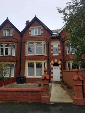 Una casa de ladrillo de dos pisos con ventanas salientes, una puerta en arco y un pequeño jardín delantero.
