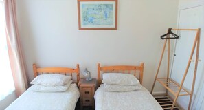 Ein Zimmer mit zwei Holzbett, einem Nachttisch mit Lampe, einem Wäscheständer aus Holz und einem Bild an der Wand.