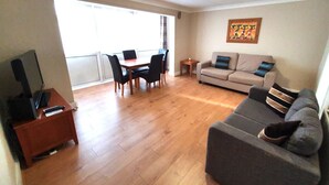 A living room with a sofa, a TV, a dining table with chairs, and a small side table.