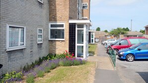 A residential building with a brick facade, a glass door entrance, and a small garden with flowers.
