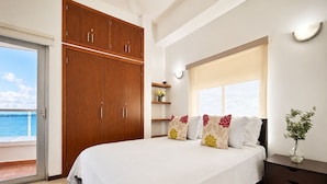 Un dormitorio con cama, armario de madera, mesita de noche y vista al mar.