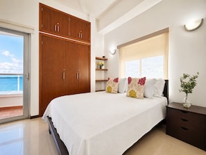 Un dormitorio con cama, armario de madera, mesita de noche y vista al mar.