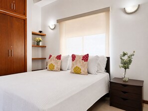 A bedroom with a bed, a nightstand, a window, and a wooden wardrobe.