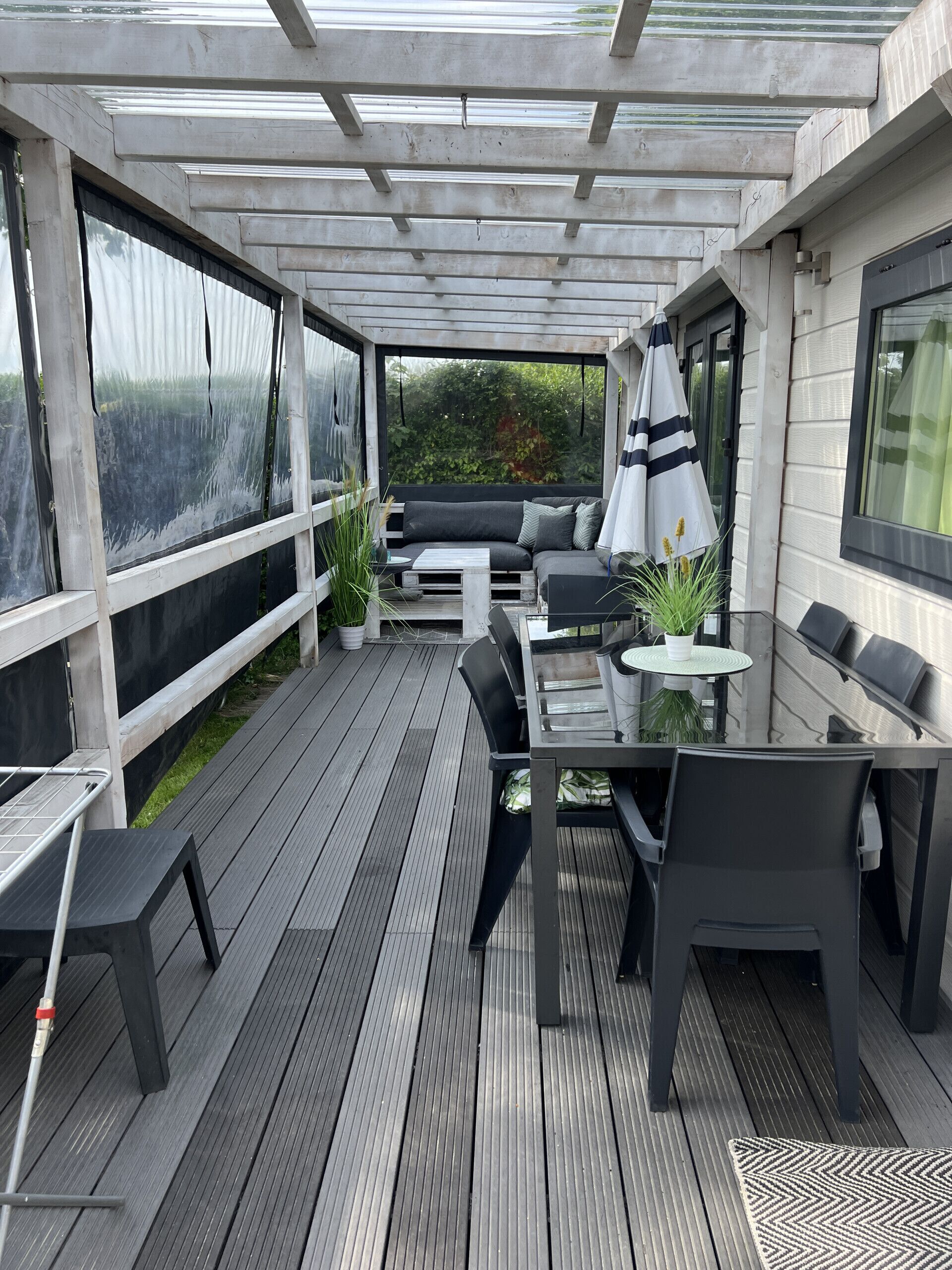 An outdoor patio with a wooden deck, a glass-top table, and black furniture.