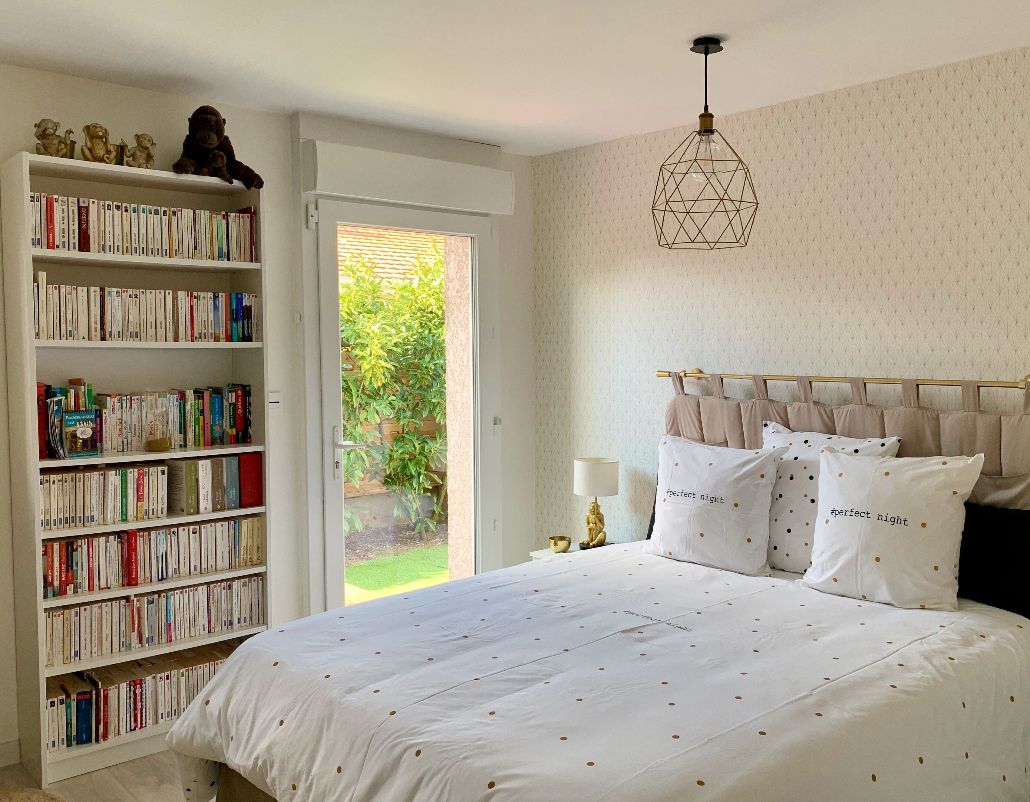 Ein Schlafzimmer mit einer großen Bücherwand, einem Bett mit gepunkteten Kissen und einer Pendelleuchte.