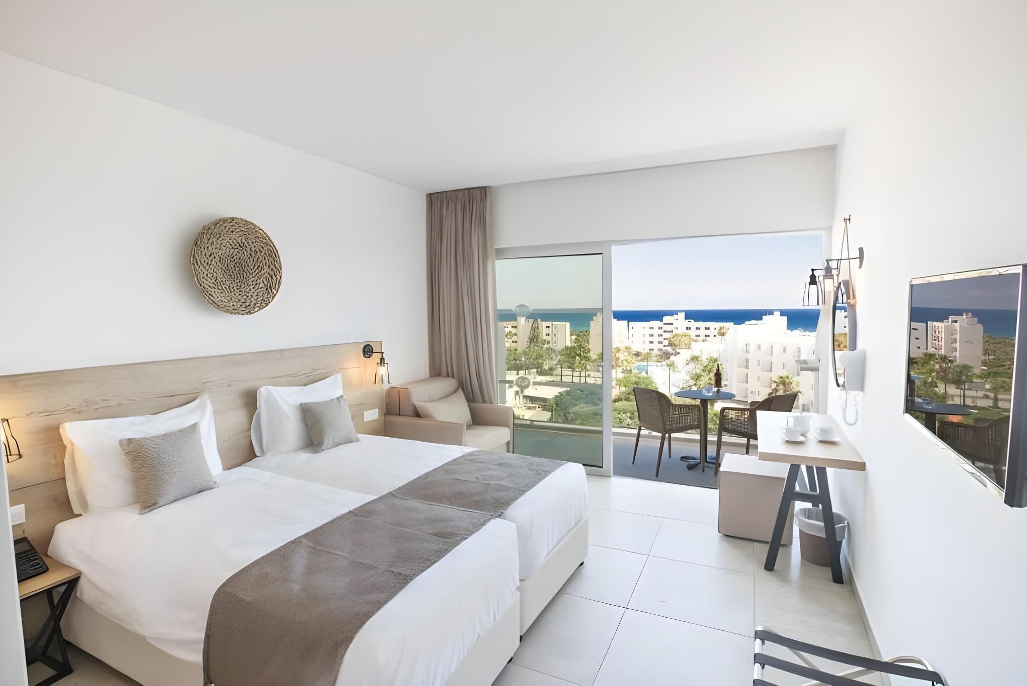 A modern hotel room with a large bed, a desk, and a balcony with a city view.