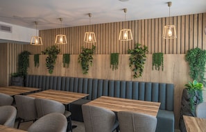 A modern restaurant interior with wooden panel walls, green plants, and pendant lighting. - Bohemian Gardens Hotel (Paralimni)