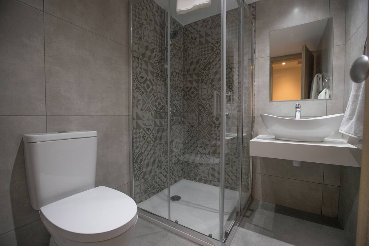 A modern bathroom with a toilet, a glass-enclosed shower, and a sink with a mirror above it.
